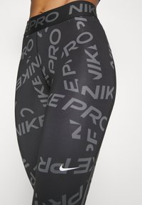 Leggings negros con un diseño gráfico que incluye el texto "NIKE" y "PRO" en diferentes tamaños. Están hechos de un material elástico y suave con una cintura cómoda.