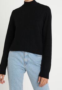 Svart kortärmad tröja med hög krage och ribbade ärmslut, tillverkad av mjukt material. I kombination med ljusblå jeans med hög midja.