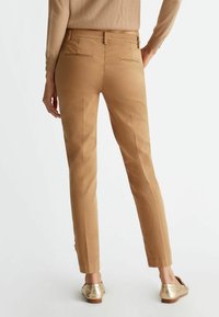 Pantaloni beige su misura con una texture morbida, due tasche posteriori e vestibilità slim. Abbinati a eleganti scarpe slip-on dorate.
