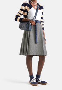 Námořnický a krémový pruhovaný kardigan přes bílý top, doplněný šedou kostkovanou sukní. Námořnické tenisky a modrá kabelka přes rameno dokončují outfit.