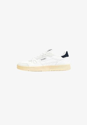 Zapatilla blanca con parte superior de ante y cuero, que cuenta con una suela de goma beige. Detalle en azul marino en el talón y un logotipo sencillo en el lado.