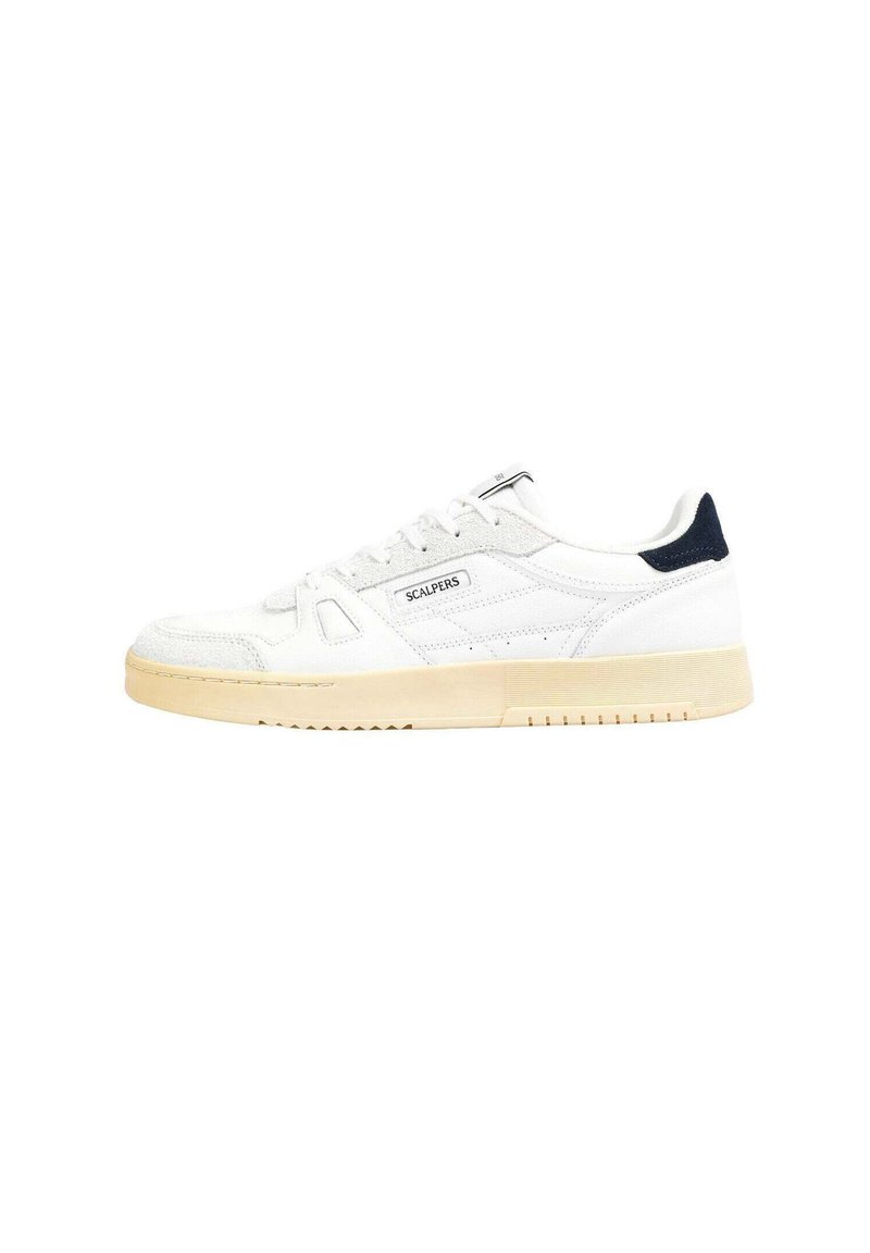 Zapatilla blanca con parte superior de ante y cuero, que cuenta con una suela de goma beige. Detalle en azul marino en el talón y un logotipo sencillo en el lado.