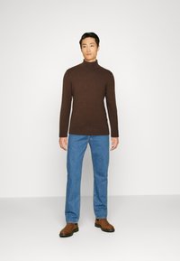 Brun genser med høy hals laget av myk stoff, kombinert med lyseblå denimjeans og brune ankelstøvler. Enkel, tettsittende design.