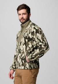Fleece-Jacke mit einem Camouflage-Muster in Grün- und Brauntönen, mit hohem Kragen, Reißverschluss und Seitentaschen.