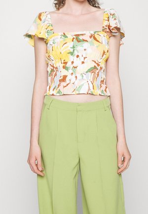 Femme portant un haut court jaune à fleurs pastel avec des manches bouffantes et un pantalon large taille haute vert clair.