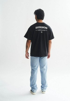 Black cotton t-shirt with large white "GOODBOIS" text on back, paired with light blue denim jeans and black sneakers. Plain background.