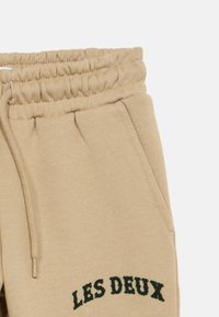 Μπεζ φόρμες με ελαστική μέση, διαθέτουν πλαϊνές τσέπες και κεντημένο το "LES DEUX" σε πράσινο κοντά στο τελείωμα. Μαλακή υφή από βαμβακερό μείγμα.
