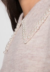 Rosa Strickpullover mit einem Kragen, der mit einer Reihe dekorativer Perlen verziert ist. Der Pullover weist einen strukturierten Stoff und subtile Farbvariationen auf.