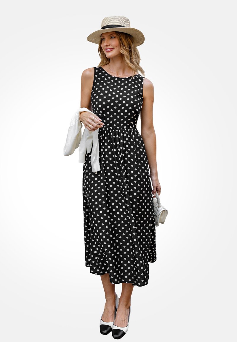 Czarna sukienka w kropki z dopasowanym topem i zwiewnym dołem, w połączeniu z kapeluszem słomkowym i białym swetrem zawieszonym na ramieniu. Czarno-białe buty.
