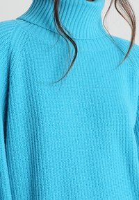 Pull en maille côtelée bleu clair à col roulé avec un design en tricot texturé. Manches longues avec une coupe décontractée, mettant en avant le tissu extensible.