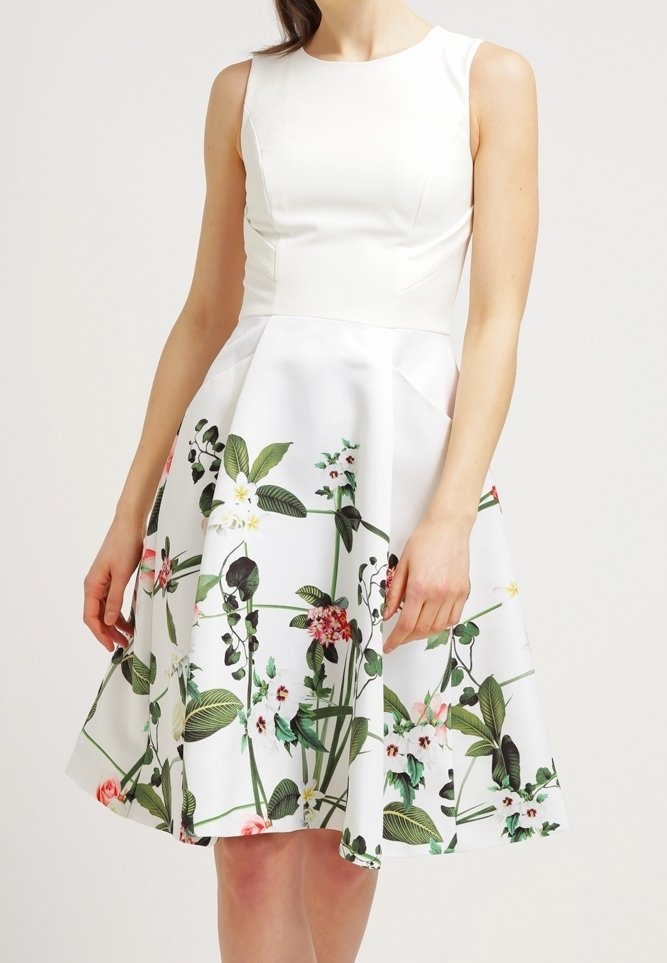 Robe blanche sans manches avec un corsage ajusté et une jupe évasée, ornée d'un imprimé floral coloré comportant diverses fleurs et des feuilles vertes.