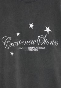 Sort bomulds-T-shirt med hvid tekst, der lyder "Create new Stories", med sølvaccenter omgivet af hvide stjernetegninger.