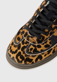 Sneaker con stampa leopardata in pelliccia marrone e nera, lacci neri e bordo in gomma scura su uno sfondo bianco.