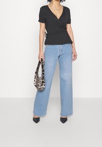 Svart omlottopp med korta ärmar, kombinerad med ljusblå vida jeans. Accessoarer med en handväska i leopardmönster och svarta spetsiga klackar.