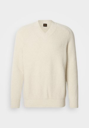 Sweater tricotado creme com decote em V, apresentando textura canelada, mangas longas e um corte descontraído. Etiqueta do logo visível na gola.