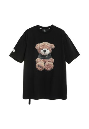 Camiseta negra de manga corta con un osito de peluche detallado que lleva un jersey oscuro impreso en el frente, y un pequeño parche en la manga izquierda.
