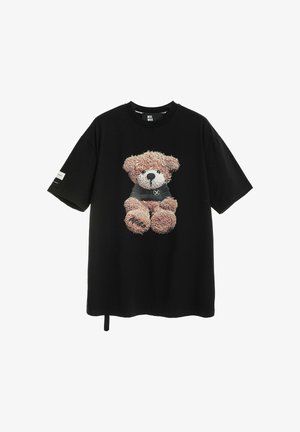 Camiseta negra de manga corta con un osito de peluche detallado que lleva un jersey oscuro impreso en el frente, y un pequeño parche en la manga izquierda.