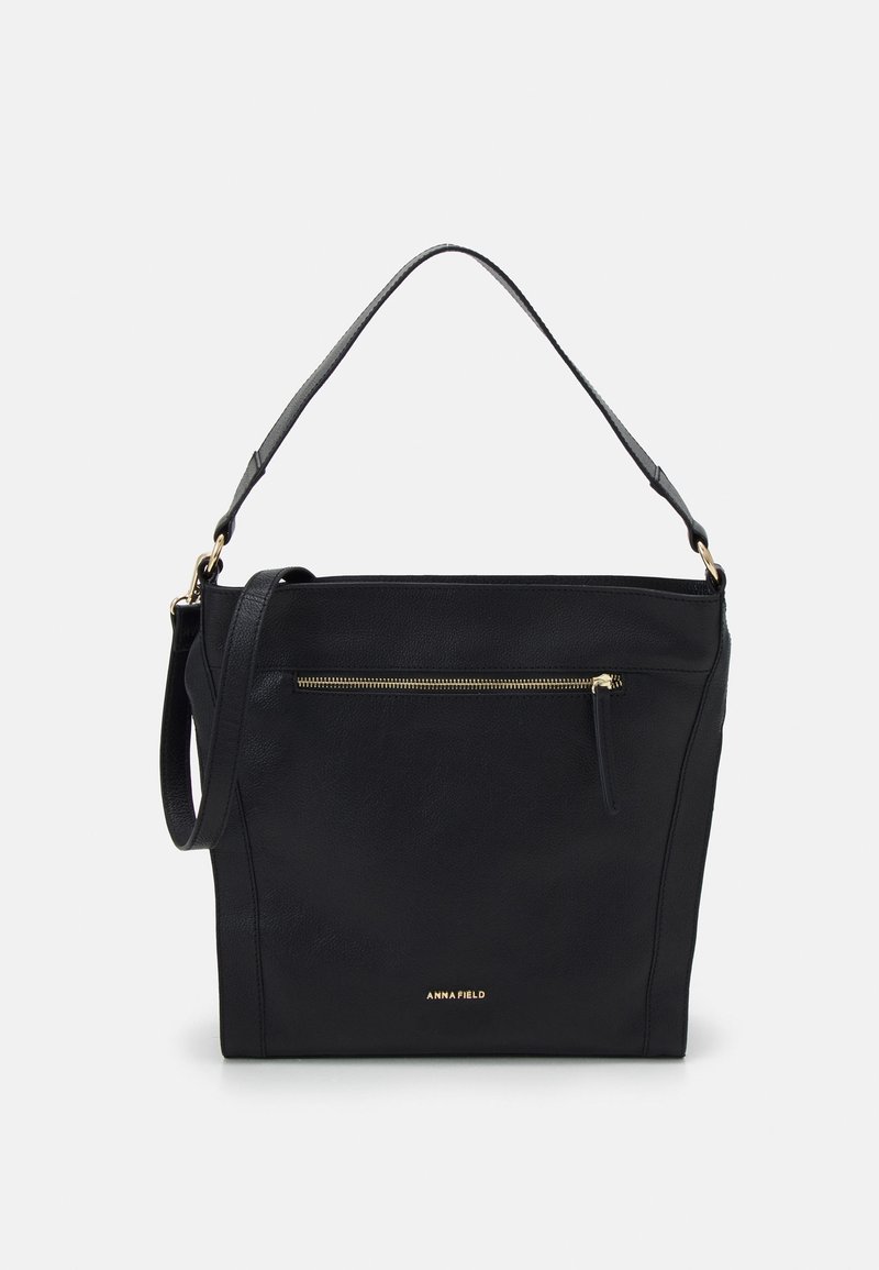 Sac à main en cuir noir avec une anse, poche avant zippée, logo doré discret "Anna Field" et design minimaliste sur fond neutre.
