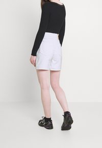 Valkoiset farkkushortsit, joissa on korkea vyötärö, kaksi takataskua ja kevyesti kuvioitu pinta, yhdistetty mustaan pitkähihaiseen yläosaan. Mukana mustat lenkkarit.