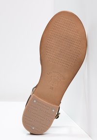 Sole di sandalo in pelle, marrone chiaro con un motivo testurizzato. Presenta marchi e dettagli della taglia impressi sul fondo. Design minimalista.