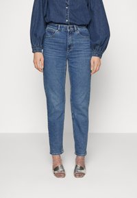 Ljusblå högmidjade jeans med rak ben, gjorda av denim. Bärs med en mörk denimskjorta och silverfärgade klackar med remmar.