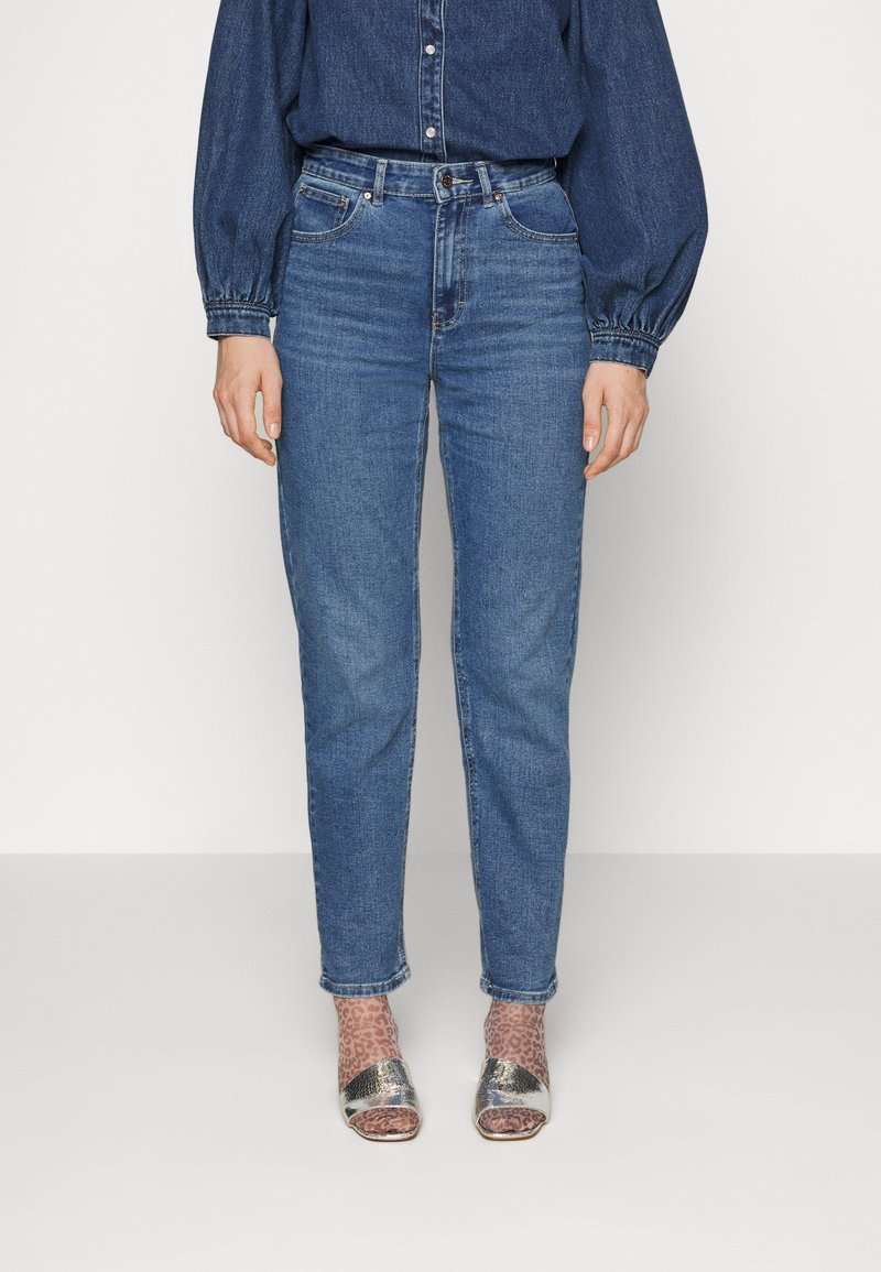 Ljusblå högmidjade jeans med rak ben, gjorda av denim. Bärs med en mörk denimskjorta och silverfärgade klackar med remmar.