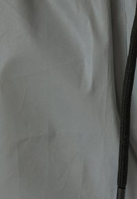 Grå vattentät tyg med en slät yta, utrustad med en svart dragsko och en subtil lyster. Designen är minimal och funktionell.