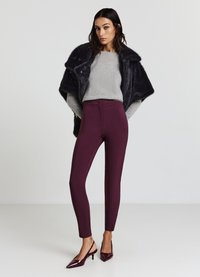 Bordeauxfarbene, taillierte Hose mit hoher Taille, kombiniert mit einem hellgrauen Pullover und einem schwarzen Kunstpelzmantel. Glänzende bordeauxfarbene, spitze High Heels.