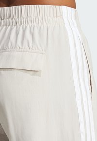 Μπέζ σορτσάκι με ελαστική μέση και τσέπη πατς. Τρεις λευκές κάθετες ρίγες προσθέτουν αντίθεση στο ελαφρύ ύφασμα.