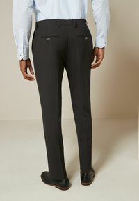Pantalons noirs formels avec une coupe slim, dotés d'un devant plat, de poches arrière avec des boutons et d'une texture lisse. Associés à des chaussures noires.