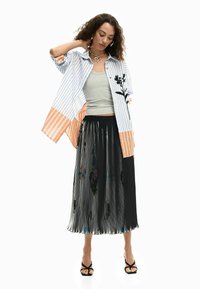 Triibuline särk lillemustriga, oranžid aktsendid; hall tanktop; volditud must seelik läikiva viimistlusega; mustad rihmikud sandaalid.