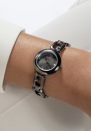 Orologio da polso rotondo di colore nero con un cinturino metallico lucido caratterizzato da collegamenti rettangolari e un quadrante testurizzato con il nome del brand al centro.