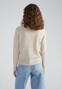 Beiger Wollpullover mit geripptem Saum und Bündchen, mit entspannter Passform und subtiler Textur. Kombiniert mit hellblauen, locker sitzenden Jeans.