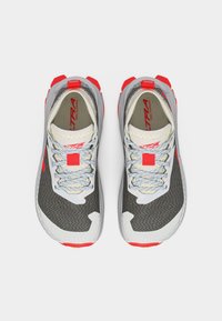 Ζευγάρι γκρι και λευκά παπούτσια για τρέξιμο σε μονοπάτια με κόκκινες λεπτομέρειες και ανοιχτογκρι κορδόνια, φαίνονται από πάνω πάνω σε λευκό φόντο.