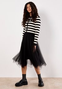 Cardigan lavorato a maglia a righe bianche e nere con scollatura rotonda, abbinato a una gonna in tulle nera che fluisce. Scarpe con plateau nere completano il look.