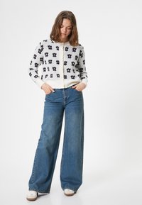 Sweter zapinany na guziki w kolorze kremowym z granatowym kwiatowym wzorem, z prążkowanymi mankietami i dołem. Połączony z niebieskimi dżinsami z szerokimi nogawkami i wysokim stanem.