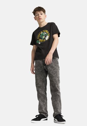 Schwarzes Baumwoll-T-Shirt mit buntem Grafikdruck, kombiniert mit grauen texturierten Jeans und schwarzen Sneakers mit weißen Sohlen.