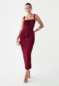 Vestido entallado burdeos con cuerpo fruncido, escote cuadrado y detalle de lazo ajustable. Tela lisa, largo hasta el suelo y diseño minimalista.