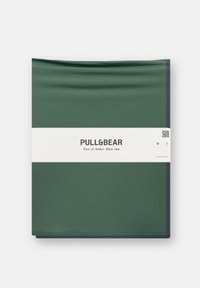 Vihreä ja tummansininen kangaspeitto, taiteltu siististi, valkoisella tarralla, jossa on brändin nimi "PULL&BEAR" ja teksti "Kaksi on parempi kuin yksi."