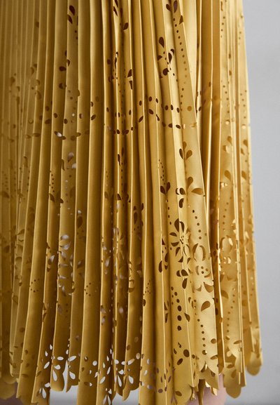 Fustă plissetată de culoare muștar, cu modele florale tăiate complicat pe margine și textură netedă pe întreaga țesătură.