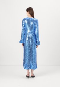 Duga, uska haljina prekrivena sjajnim plavim šljokicama. Ima širom rukave i zatvarač na leđima. Glatka tekstura s volanima na rubu.