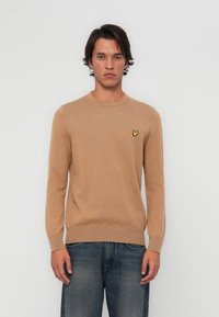 Beige kötött pulóver, kerek nyakkivágással és hosszú ujjakkal. A bal mellen egy kis sárga logó található. Puha anyagból készült.