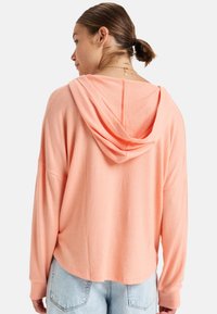 Oversized, lichtgewicht hoodie van zachte koraalkleurige stof met een achternaad en een grote, gedrapeerde capuchon. Gecombineerd met losse, lichtblauwe denim.