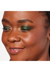 Primo piano di un volto che mette in risalto un ombretto verde iridescente, un accento dorato sulle palpebre, labbra lucide e pelle liscia con tonalità calde.