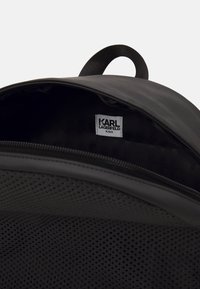 Wnętrze czarnego plecaka o gładkiej fakturze, z metką z napisem "KARL LAGERFELD KIDS" oraz detalami w siateczkowy wzór.