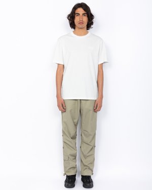 Biała bawełniana koszulka z okrągłym dekoldem i subtelnym logo, sparowana z jasnymi, khaki spodniami cargo z bocznymi kieszeniami i zatrzaskami.