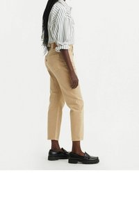 Jeans beige de talle alto con corte recto, combinados con una camisa de botones de rayas blancas y negras, y mocasines negros.