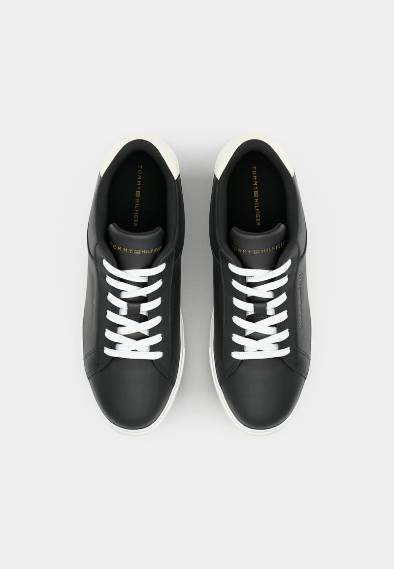 Zapatillas de cuero negro con cordones blancos, diseño de punta redonda y acentos beige en el talón. Logo dorado impreso en la lengüeta y el costado.