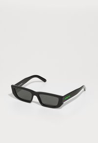 Ochelari de soare dreptunghiulari negri cu lentile închise, fabricați din plastic. Prezintă un logo verde "ARNETTE" pe brățară. Textură netedă.