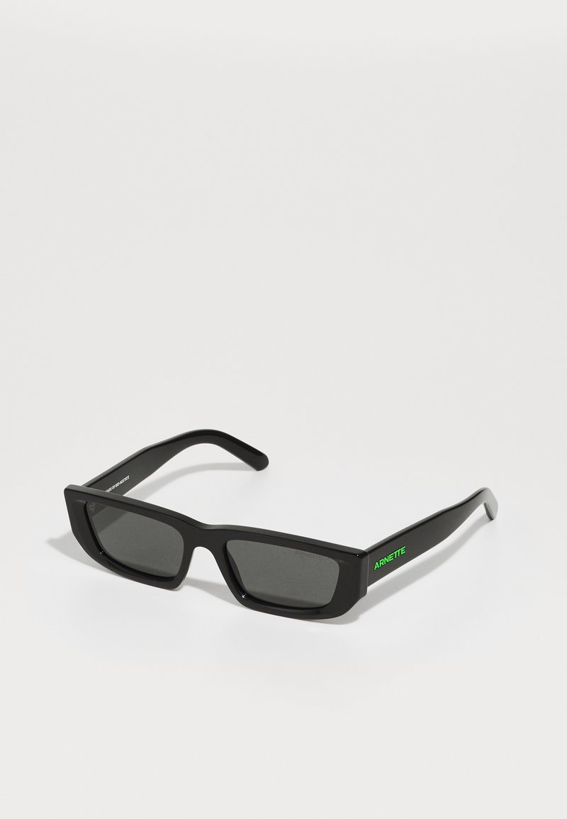 Ochelari de soare dreptunghiulari negri cu lentile închise, fabricați din plastic. Prezintă un logo verde "ARNETTE" pe brățară. Textură netedă.